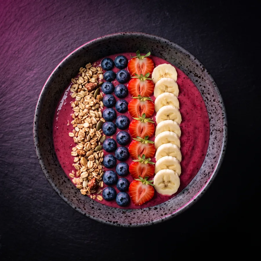 Beeren-Bowl in Pink mit Erdbeeren, Heidelbeeren, Bananenscheiben und Granola in Reihen.